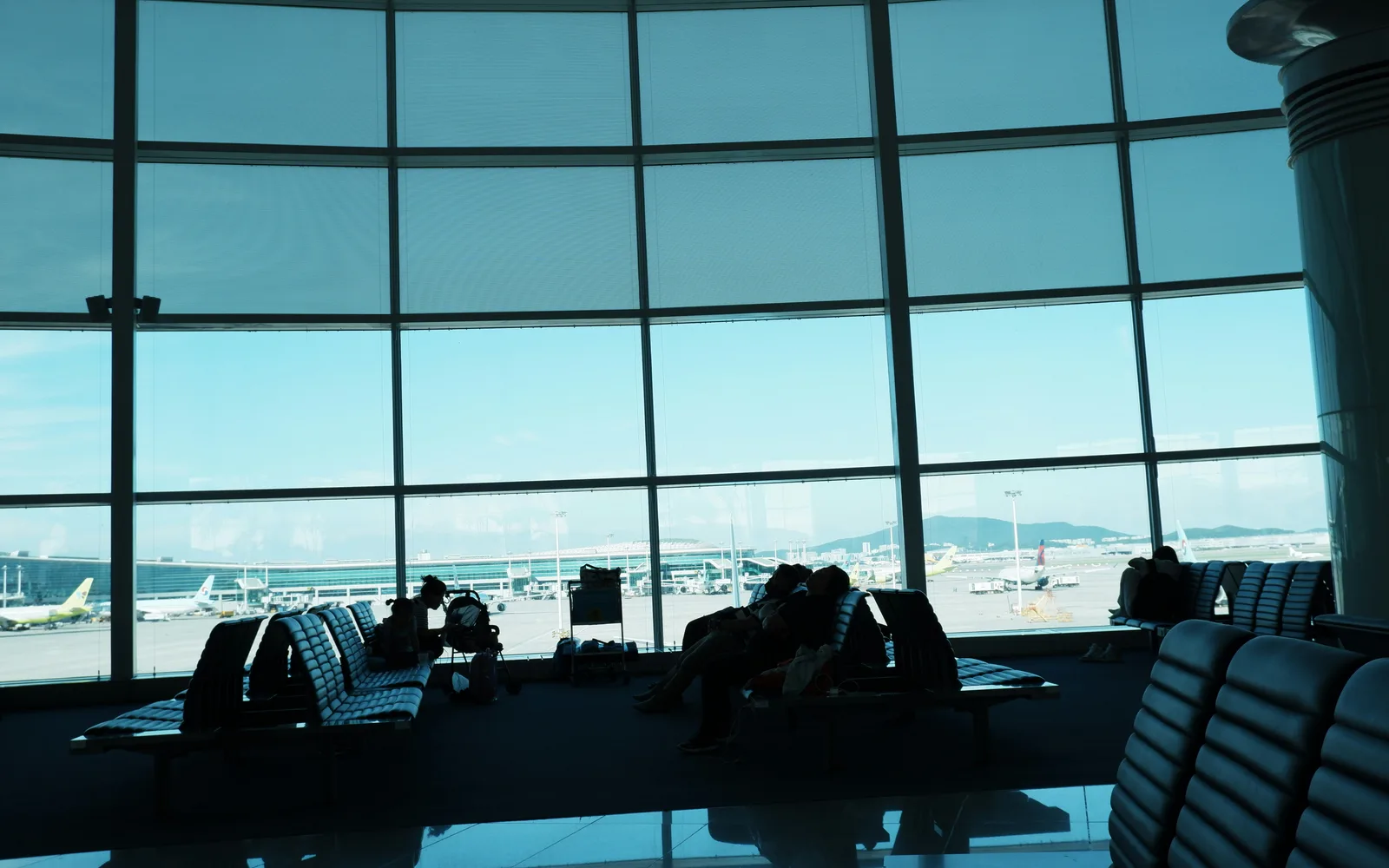 Passengers resting beside a large window overlooking the Incheon Airport apron
