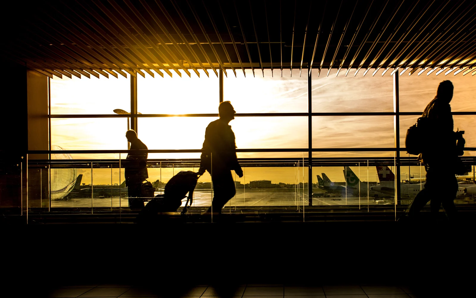 Travelers carrying luggage through an airport terminal at sunset