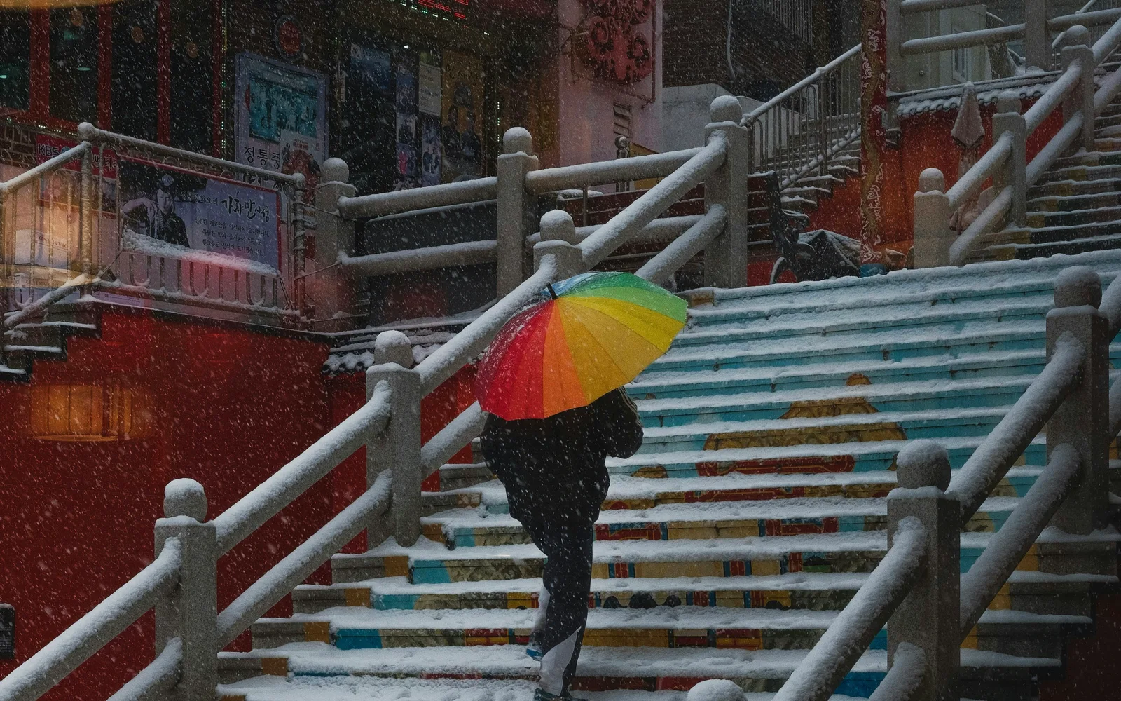 Person with a rainbow umbrella climbing snow-covered stairs in Incheon Chinatown