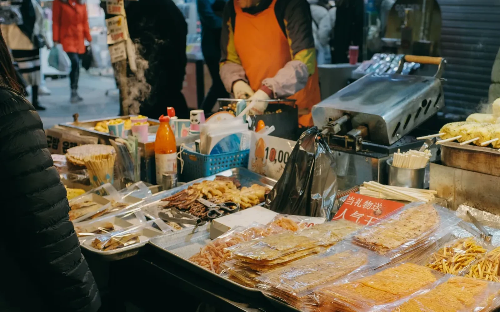 Vendor behind steamed corn and packaged snacks at a Korean market stall