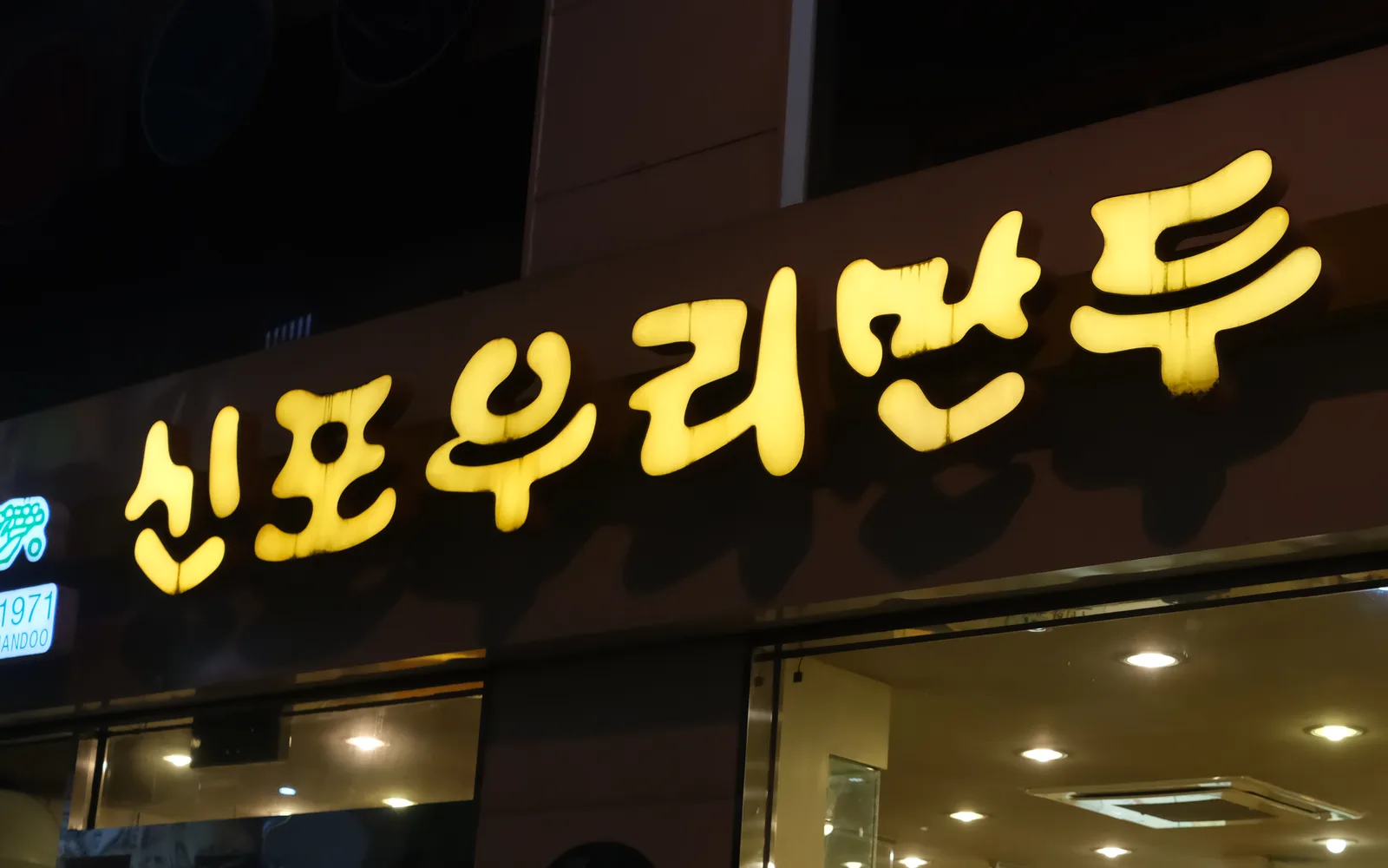 Illuminated Sinpo Woori Mandu storefront sign photographed in the Sinpo market area