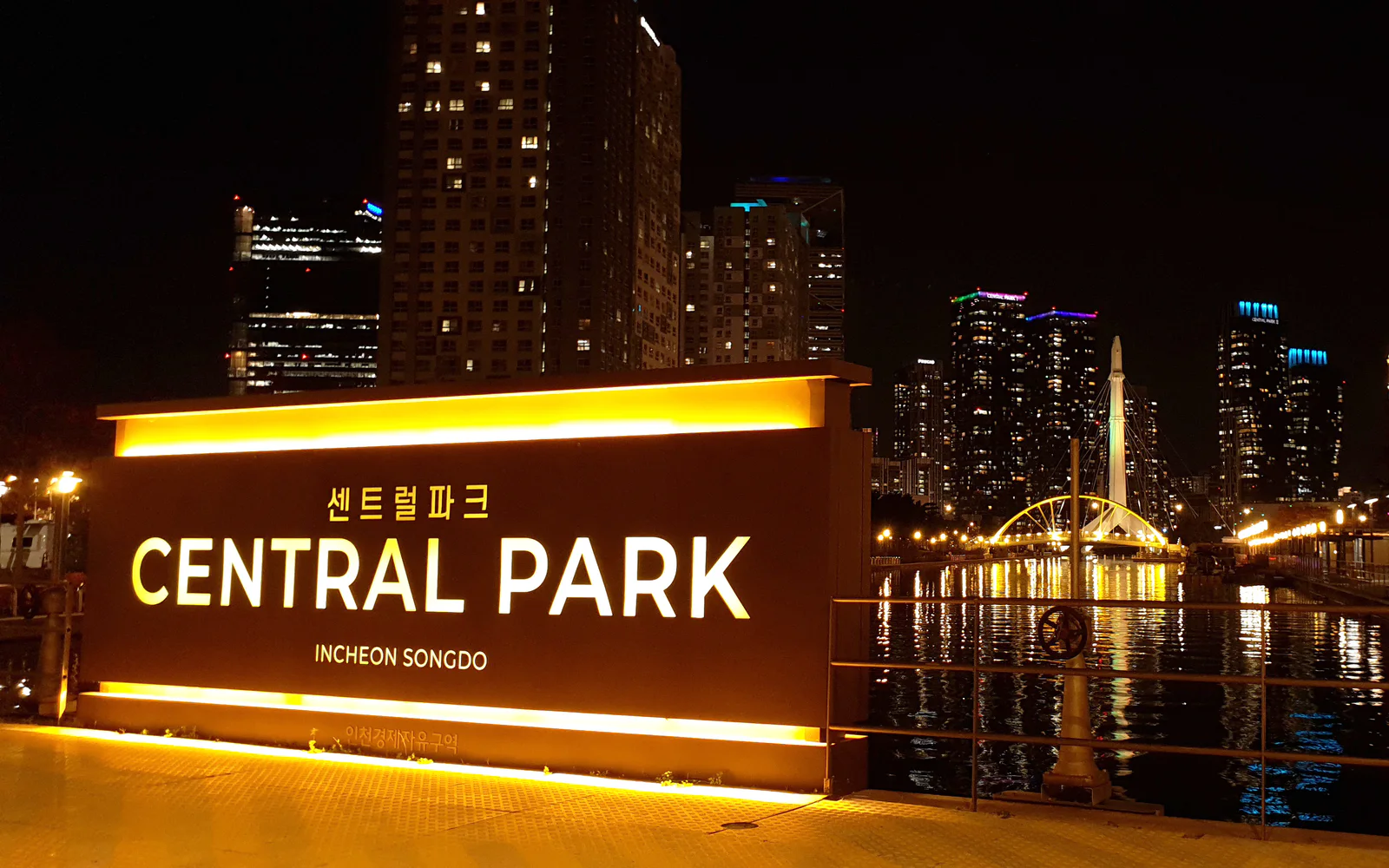 Illuminated Central Park sign beside a bridge and skyline in Songdo at night