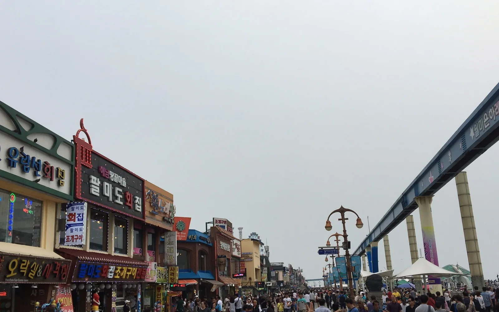 Busy Wolmido waterfront promenade lined with seafood restaurants beside an elevated rail structure