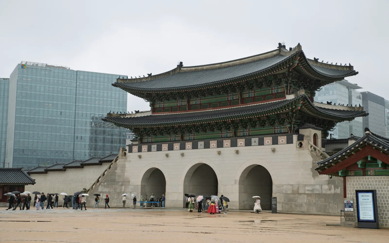 Gwanghwamun gate at Gyeongbokgung in the rain with modern buildings behind it